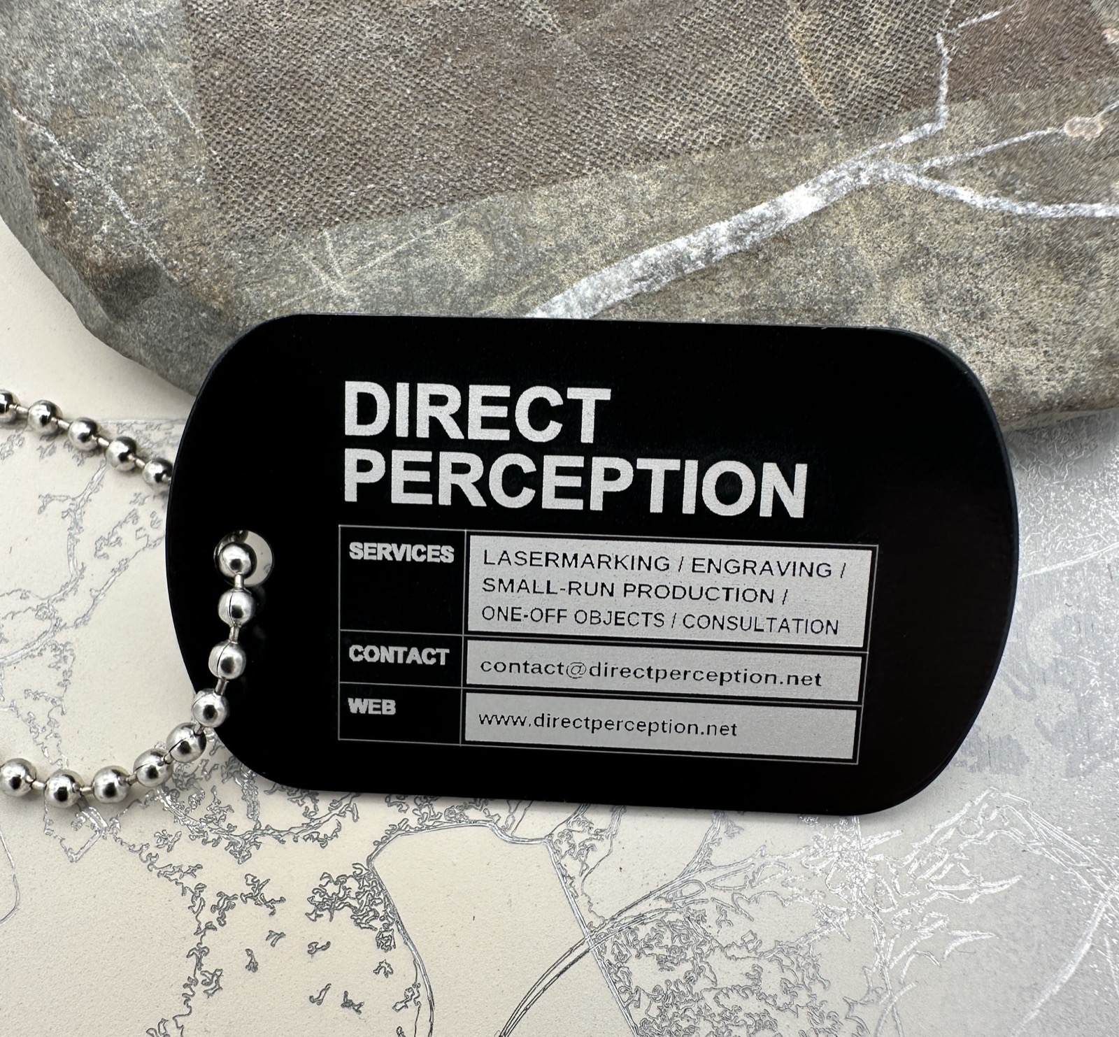 Black Direct Perception dog tag with contact details.