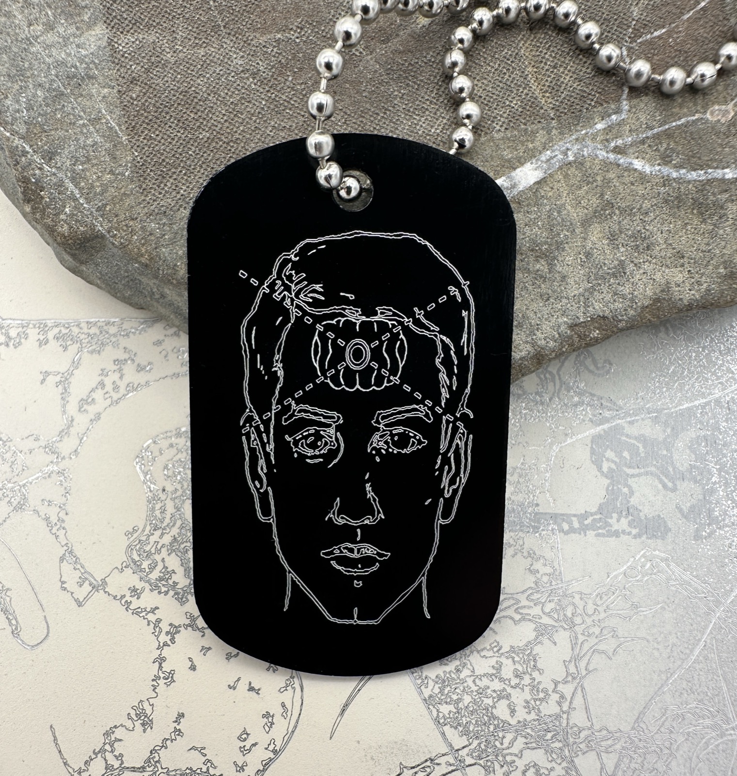 Black Direct Perception dog tag with an engraved portrait.