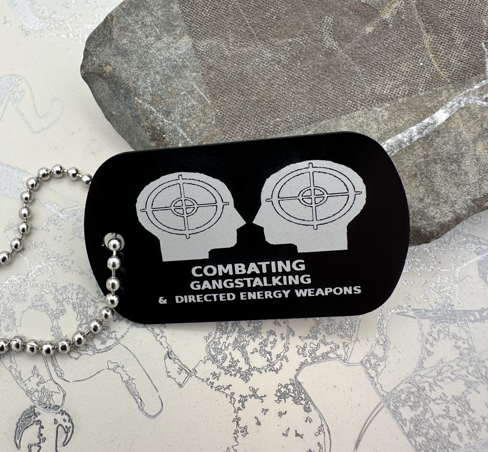 Black engraved dog tag with two head silhouettes and Combatting Gangstalking lettering.