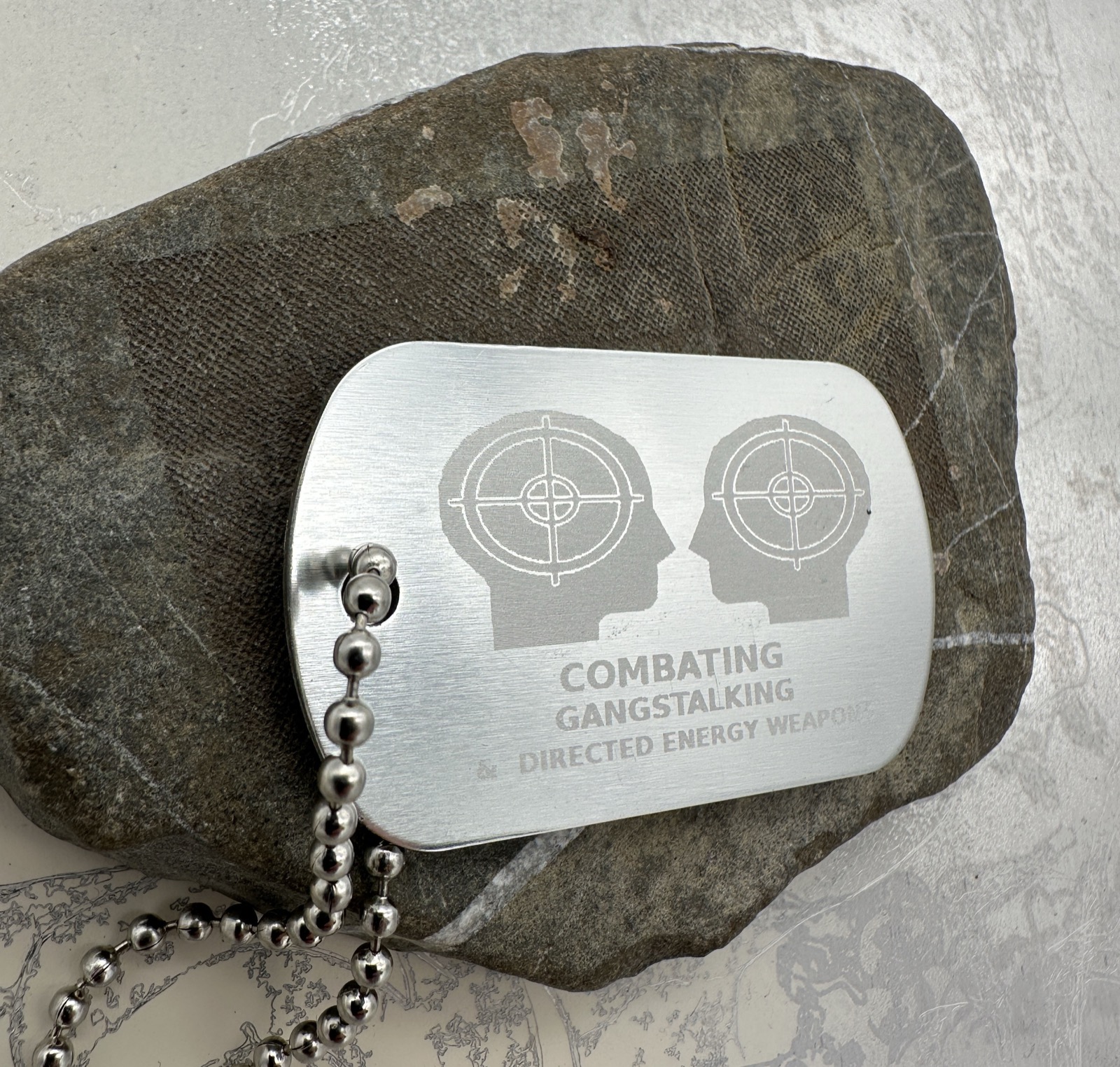 Silver-coloured engraved dog tag with two head silhouettes and lettering.