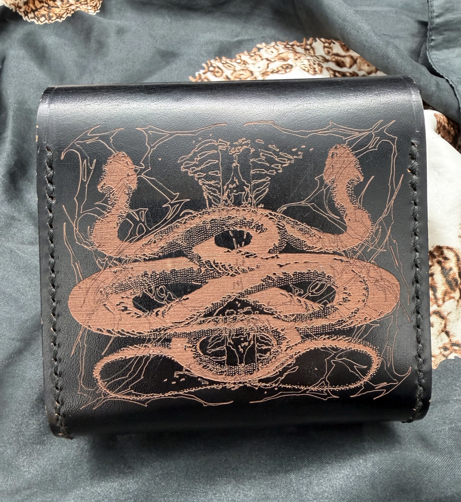 Reverse of the black leather postal case, engraved with intertwined snakes and fine anatomical and branching motifs.