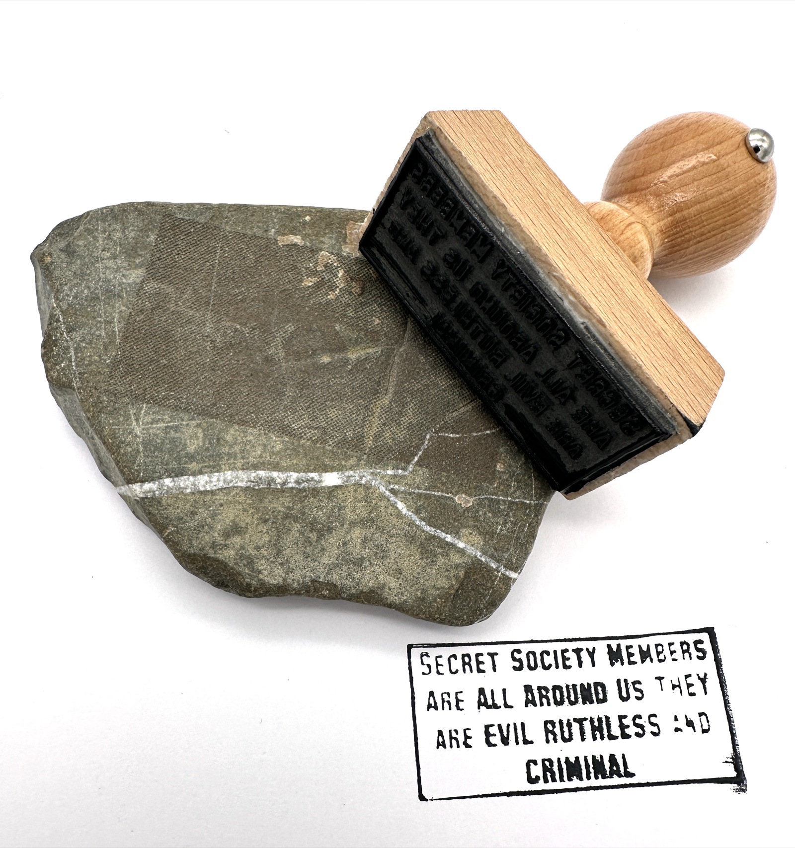 Wooden-handled rubber stamp beside its printed impression on paper.