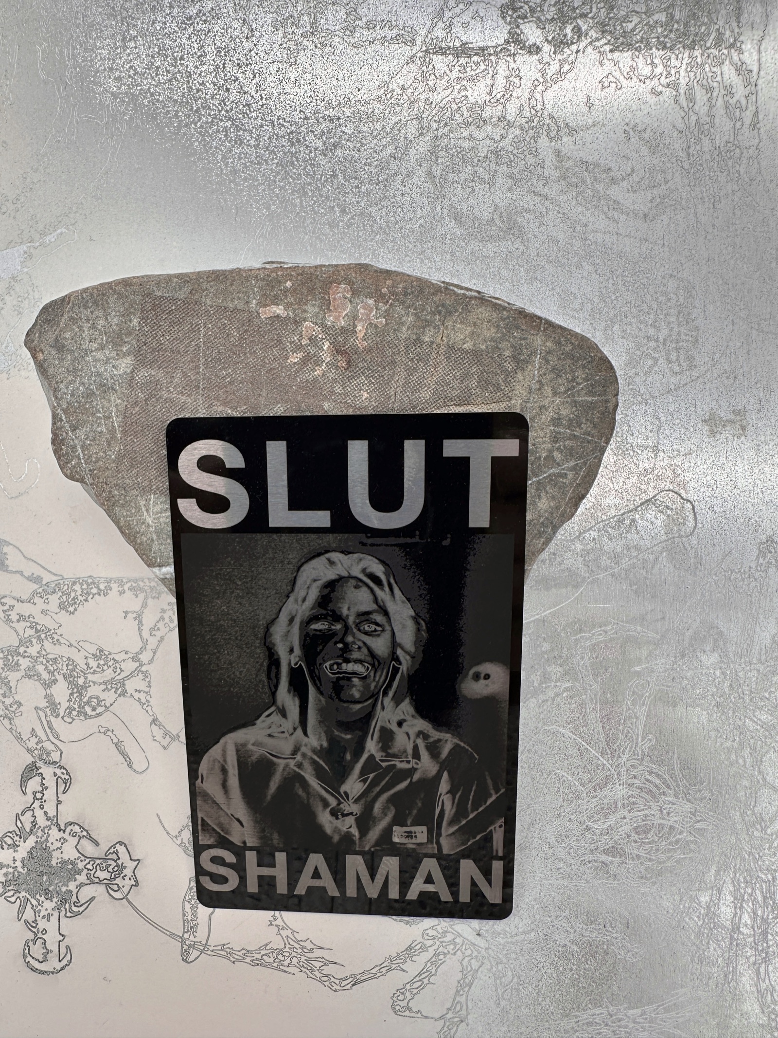 Engraved black metal card with a portrait and Slut Shaman lettering.