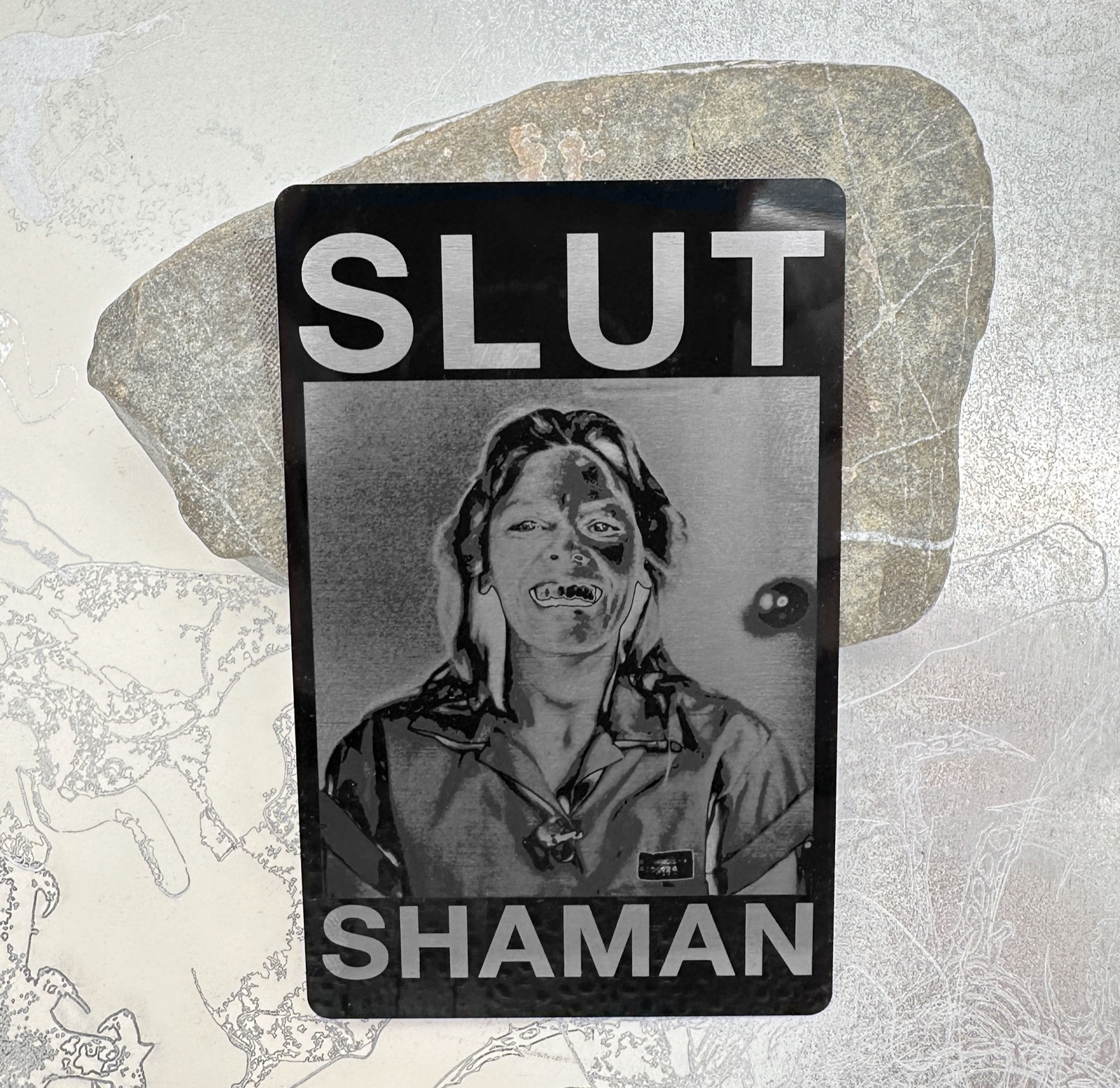 Close-up of the portrait and lettering engraved on a black metal card.